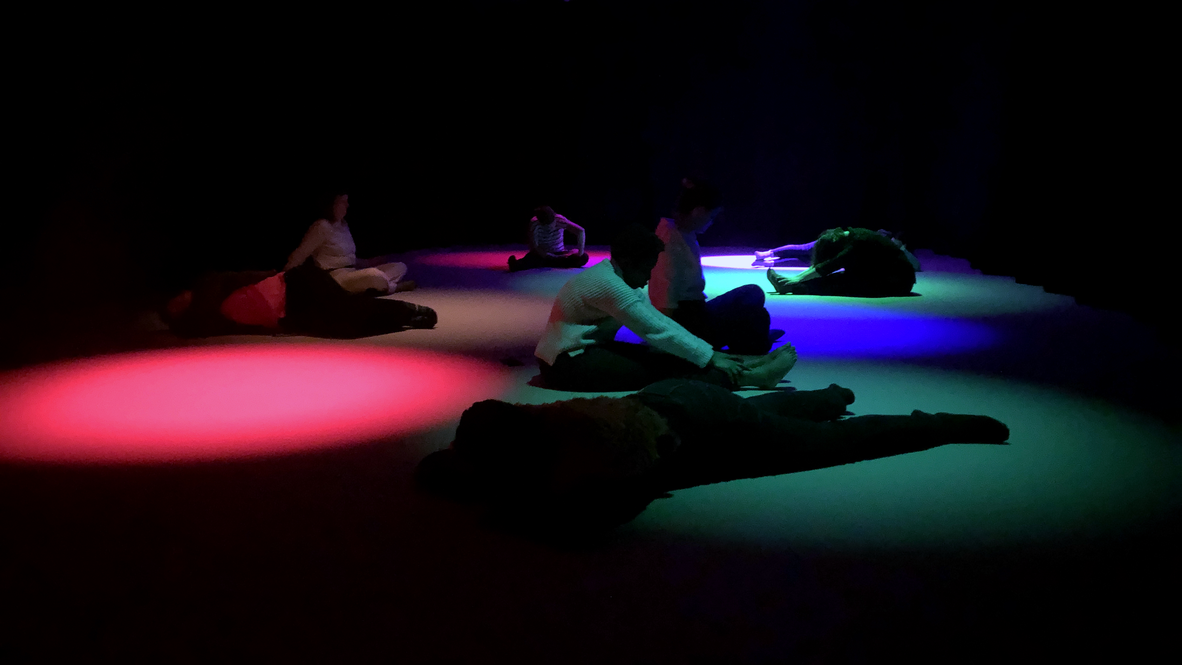 Participants sit on the floor with cyan, red, and blue light covering them and their surroundings.