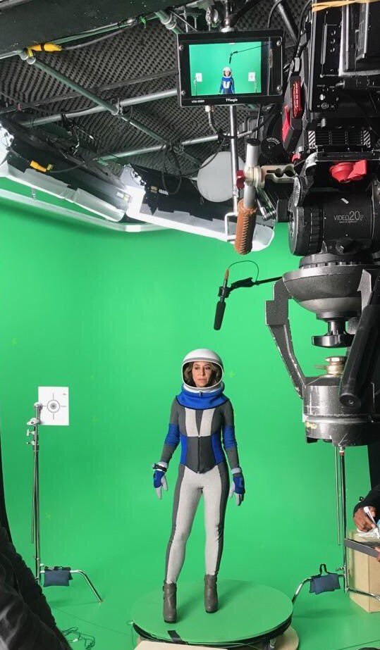 Janna Levin stands in a custom-made spacesuit in front of a camera rig and green screen