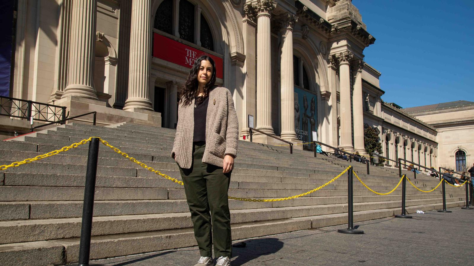 Capua standing outside of the Met's main entrance on 5th ave wearing a cardigan and army green pants.