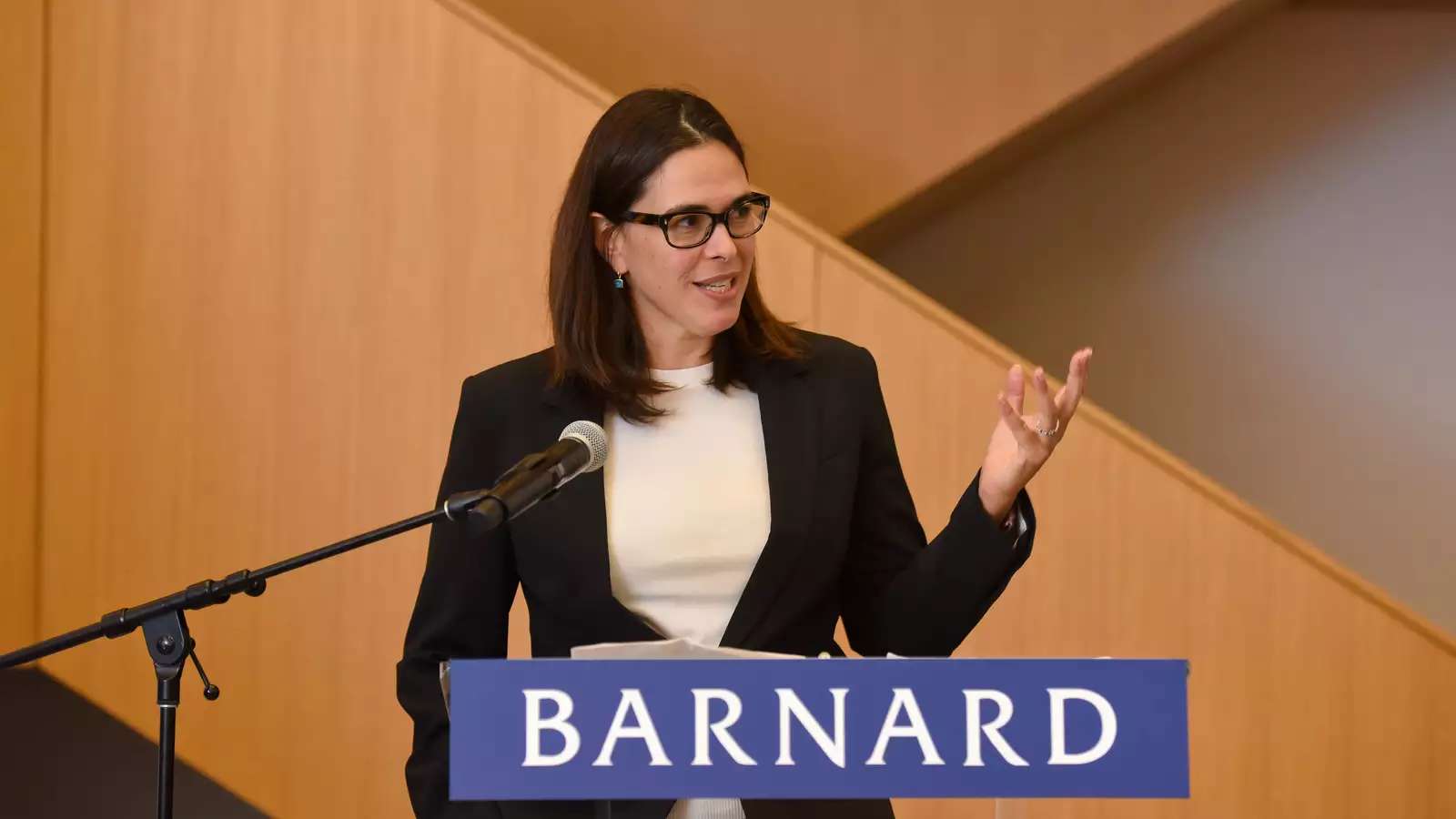 Woman with dark hair wearing dark suit jacket in front of Barnard podium