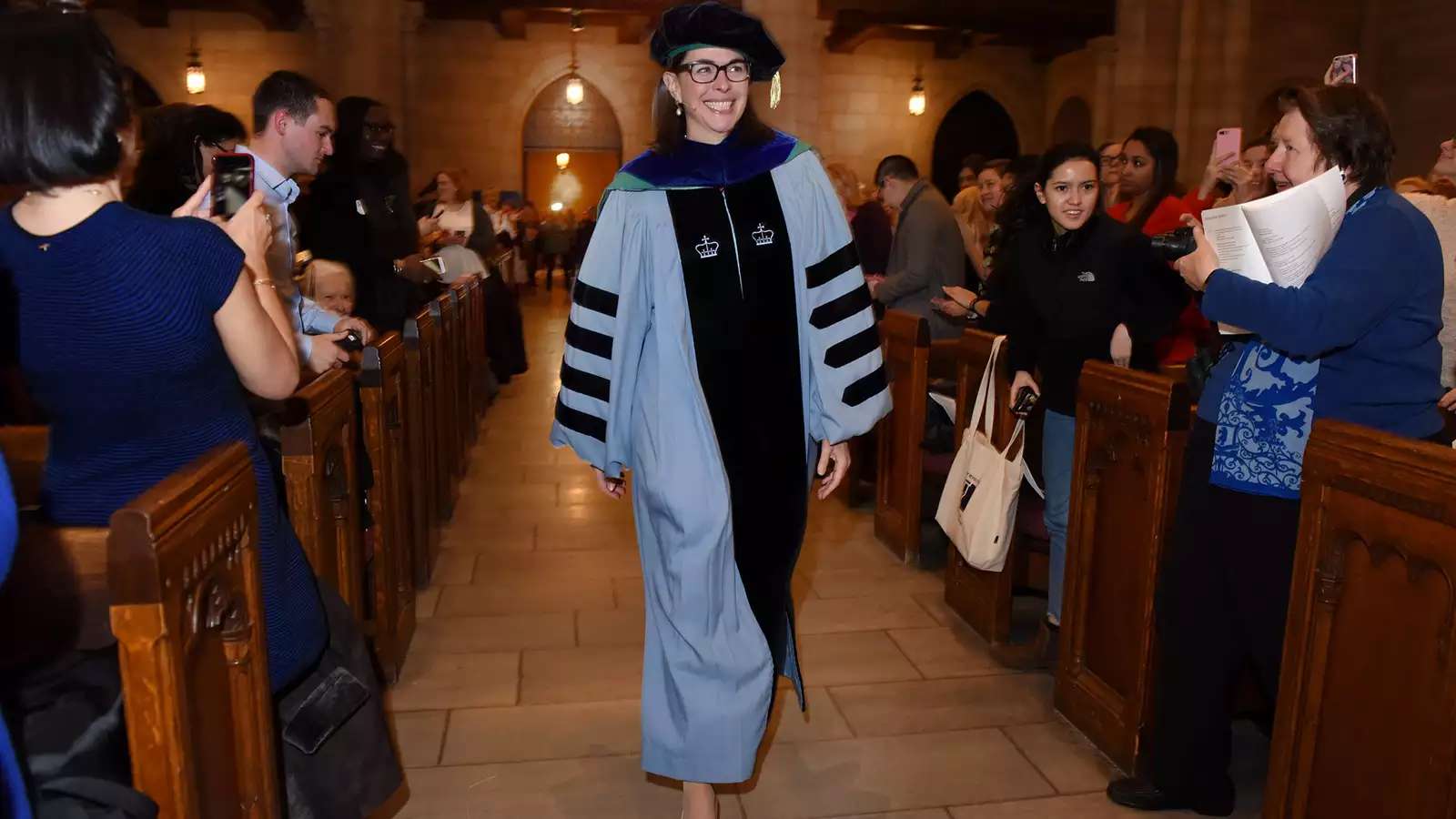 Woman in academic regalia walking down aisle.