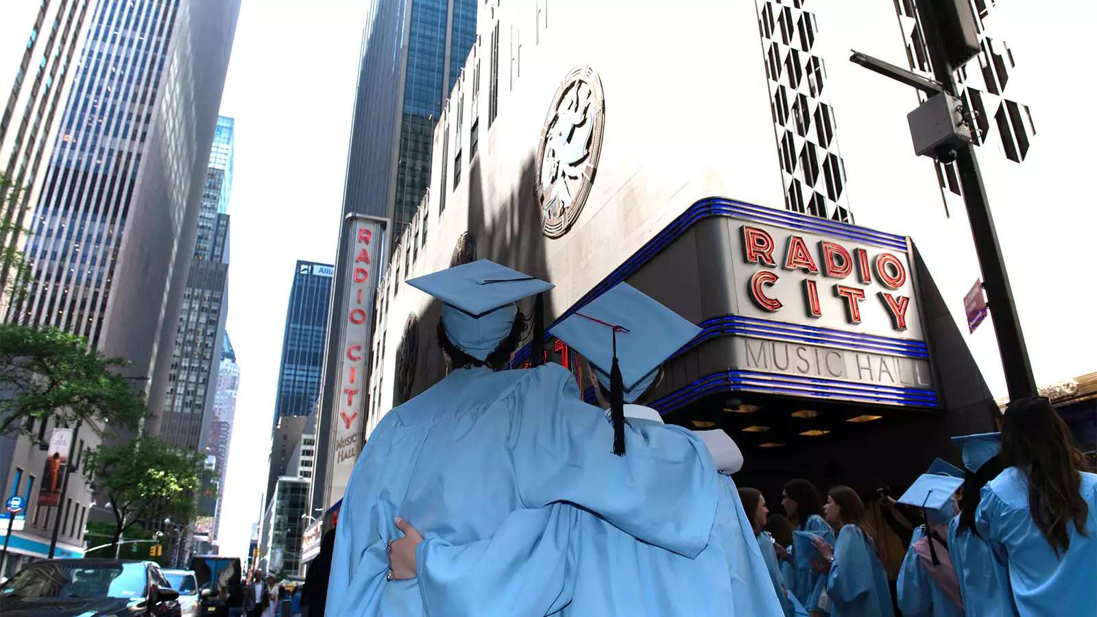 Two Barnard students in graduation regalia in front of radio city music hall