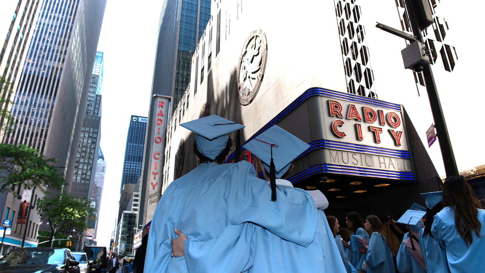 Two Barnard students in graduation regalia in front of radio city music hall