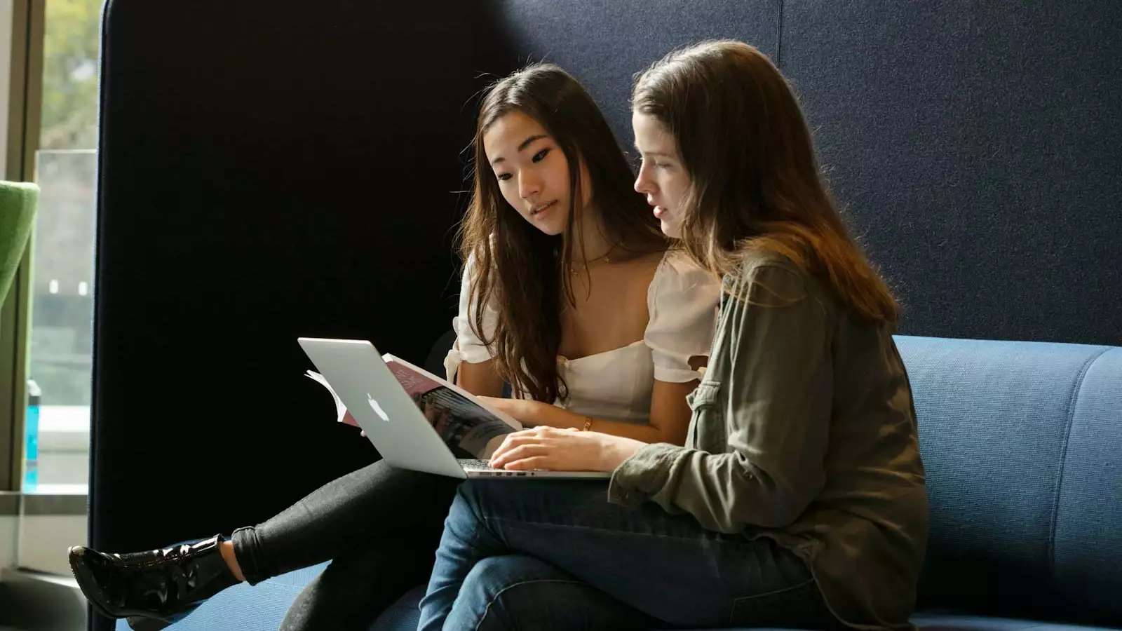 2 students on a high-backed couch, working on a laptop 