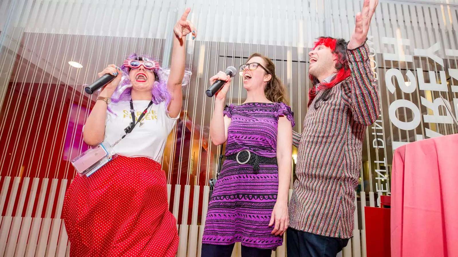 3 people in wild costumes singing in an office