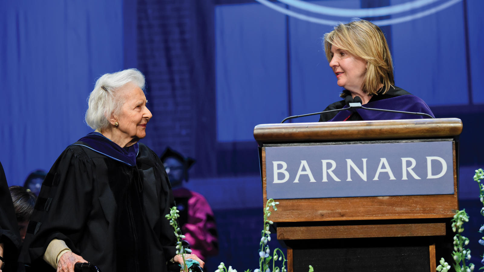 2 alumnae on stage in black academic gowns
