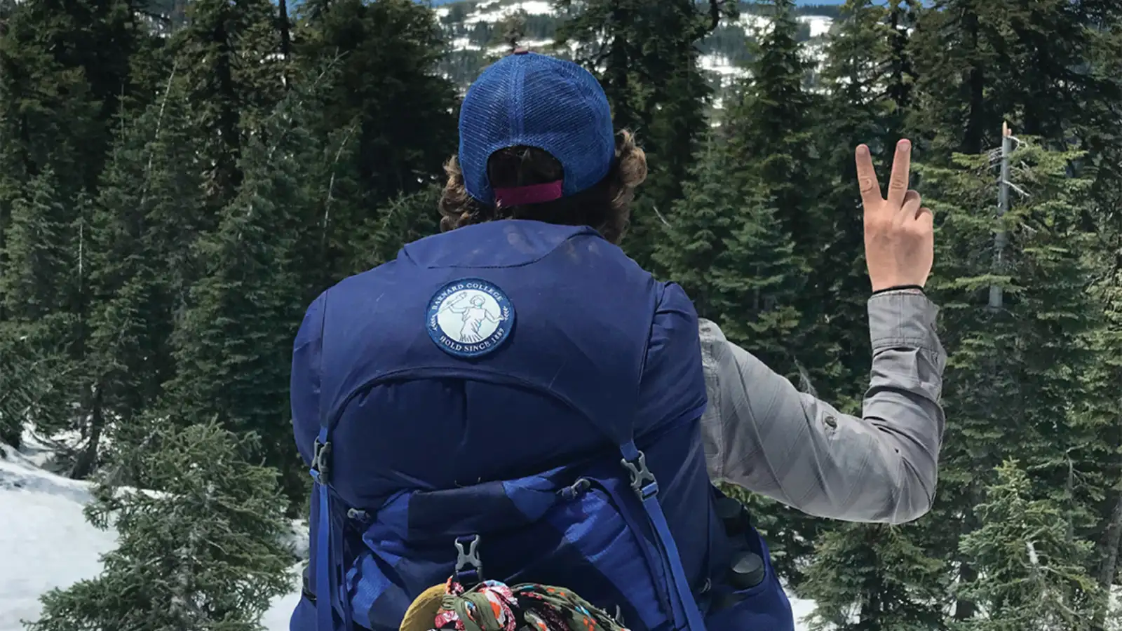 A woman wearing a hiking backpack looks over a snowy wilderness