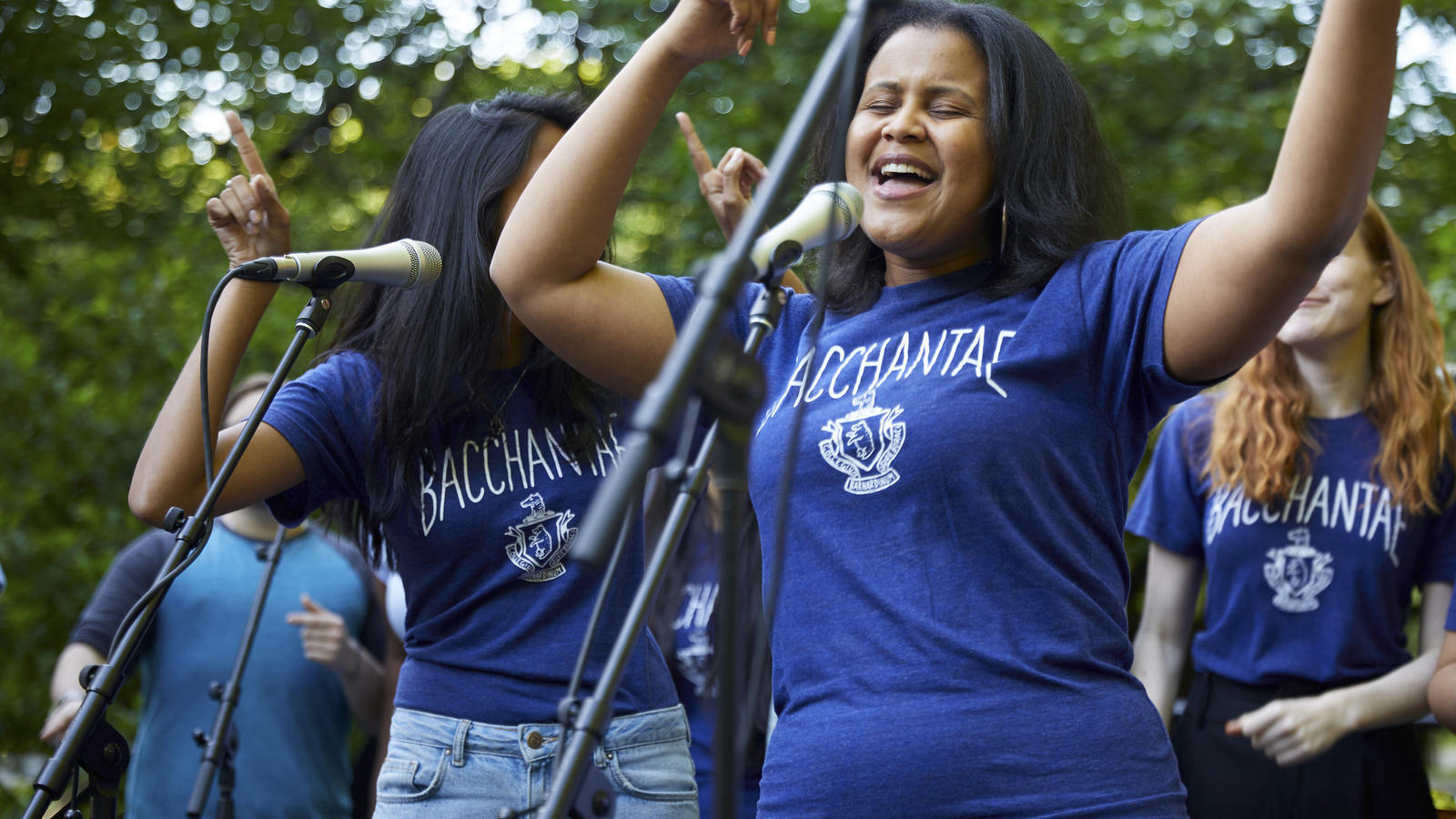 A young Black woman sings outdoors as part of the Bacchantae performance