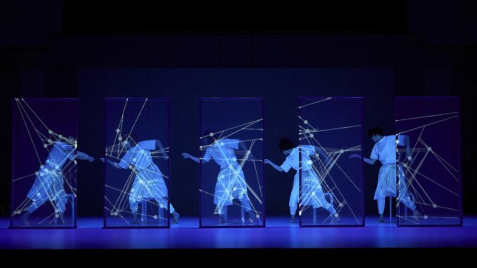5 people in white behind clear screens on a dark stage