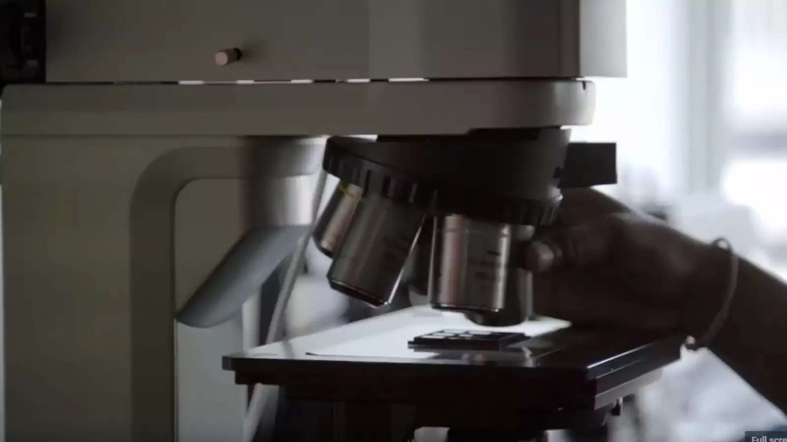 close up of a microscope and a hand positioning a slide