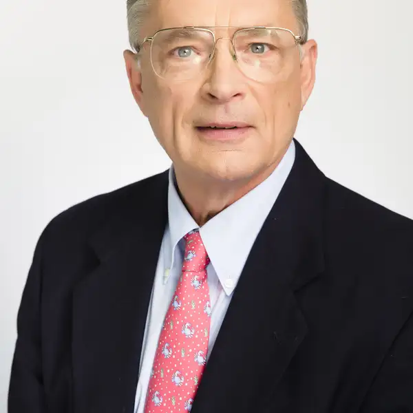 Man with with short gray hair wearing dark suit jacket, white shirt and pink tie.