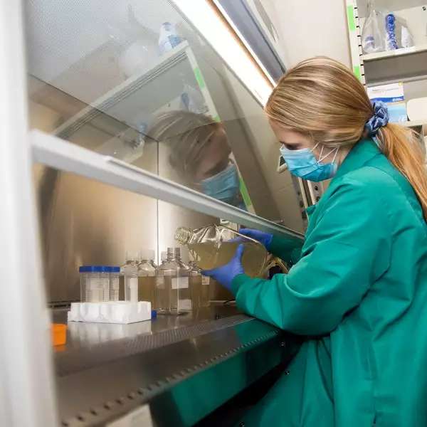 Woman in protective gear pours water from large sample jug into test tubes