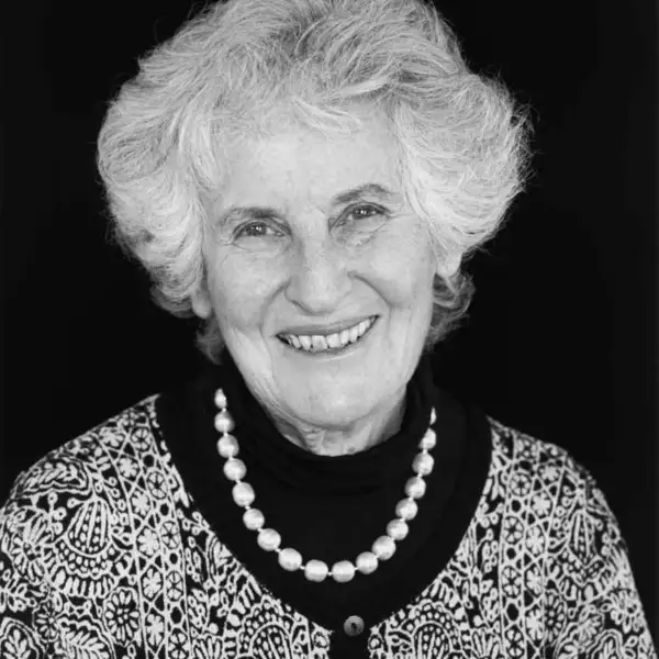 Black-and-white photo of Joan Birman facing front and wearing a black sweater and pearls with a black-and-white patterned jacket over it.