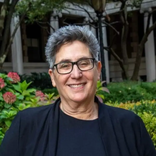 Photo of Prof. Debra Minkoff wearing a lack top with a garden behind her
