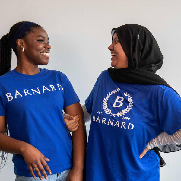 Two women looking at each other wearing blue t-shirts with Barnard logos