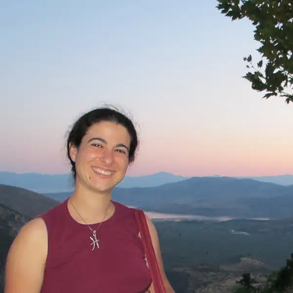 Photo of Darcy Krasne wearing a red tank top with a sunset behind her