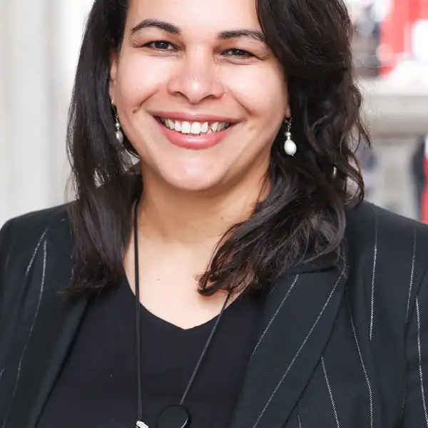 Rosa Andujar smiling at the camera wearing a black top with a blazer and small dangling pearl earrings
