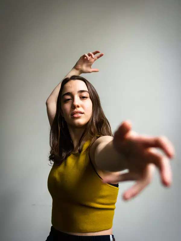 Allison Costa dancing, reaching towards the camera, wearing a yellow shirt