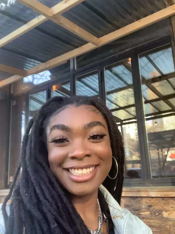 Erinma is standing outside a building with glass windows and smiling.