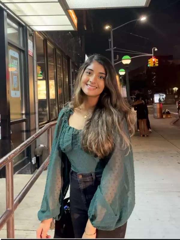 image of Noreen in a green long-sleeved shirt standing on the sidewalk and smiling