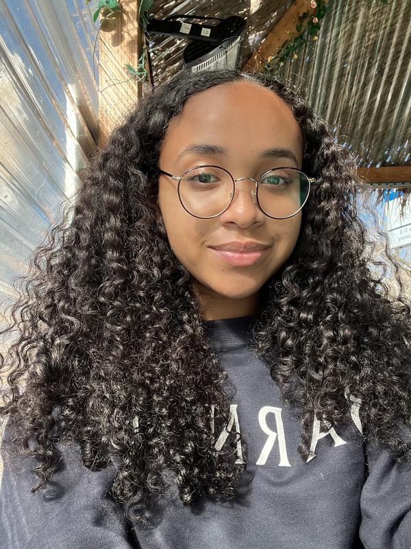 Lauren is wearing a barnard sweatshirt and glasses and smiling at the camera.
