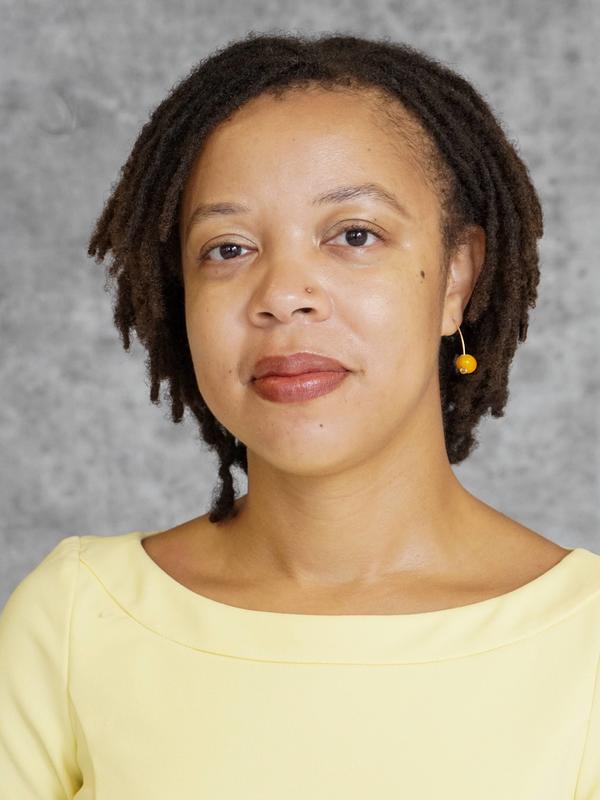 Headshot image of Dr. Amelia Simone Herbert. She has short locs and a yellow dress and looks directly into the camera.