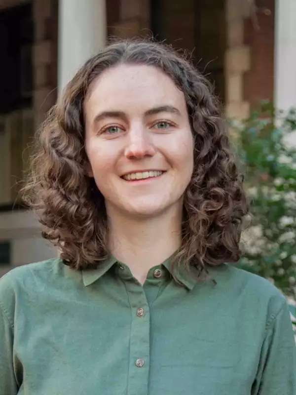 mixed background, woman smiling with brown wavy hair, sage green collared shirt