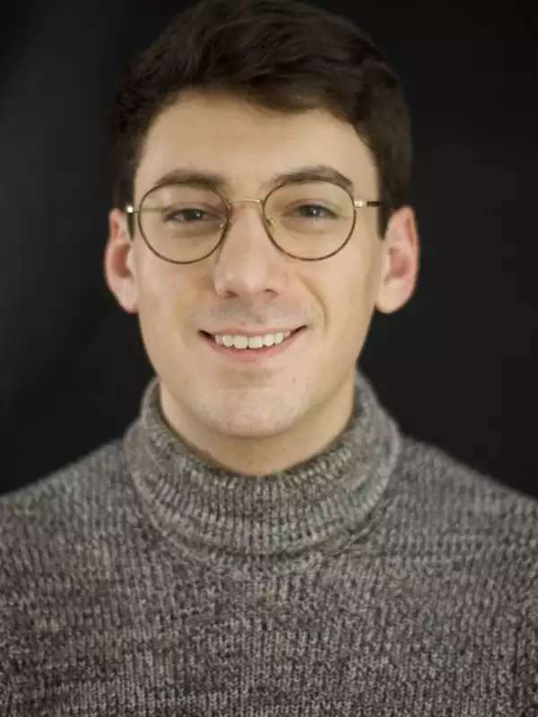 Man smiling with gray turtleneck, against black background