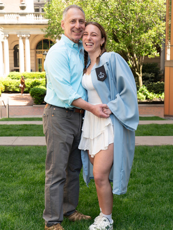 A man and a younger woman in college regalia holding hands