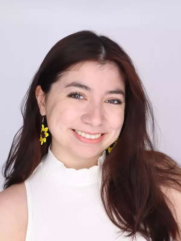 Headshot of a person with brown hair and a white shirt on an off-white background