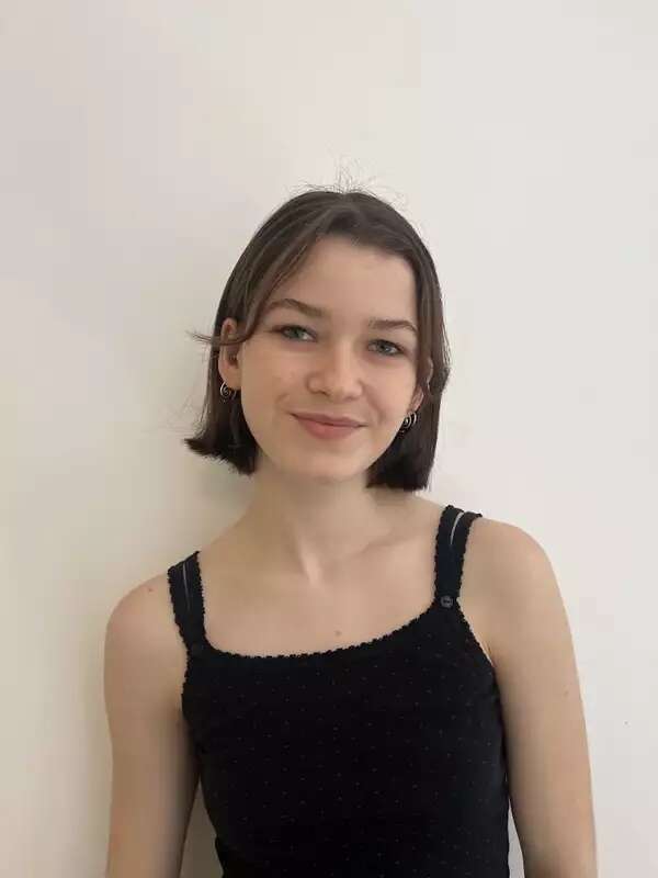 A student faces the camera while standing in front of a white wall. 