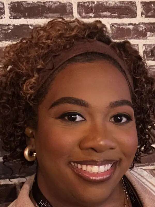 Woman with short curly highlighted hair and gold earrings smiling