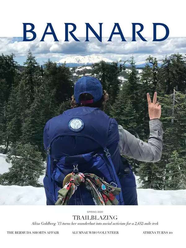 A woman wearing a hiking backpack looks over a snowy wilderness