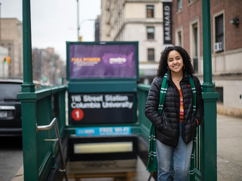 A young woman stands in front of the train entrance.