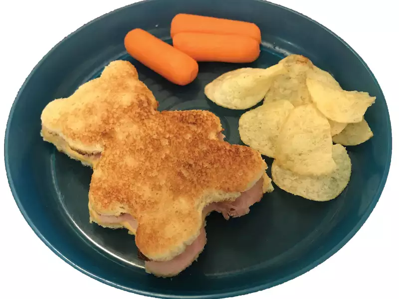 A picture of sandwich shaped like bear with carrots and potato chips.