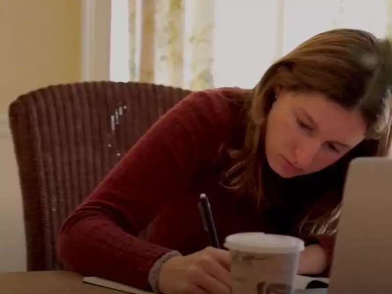 Young woman writing in a notebook, sitting in front of her laptop.