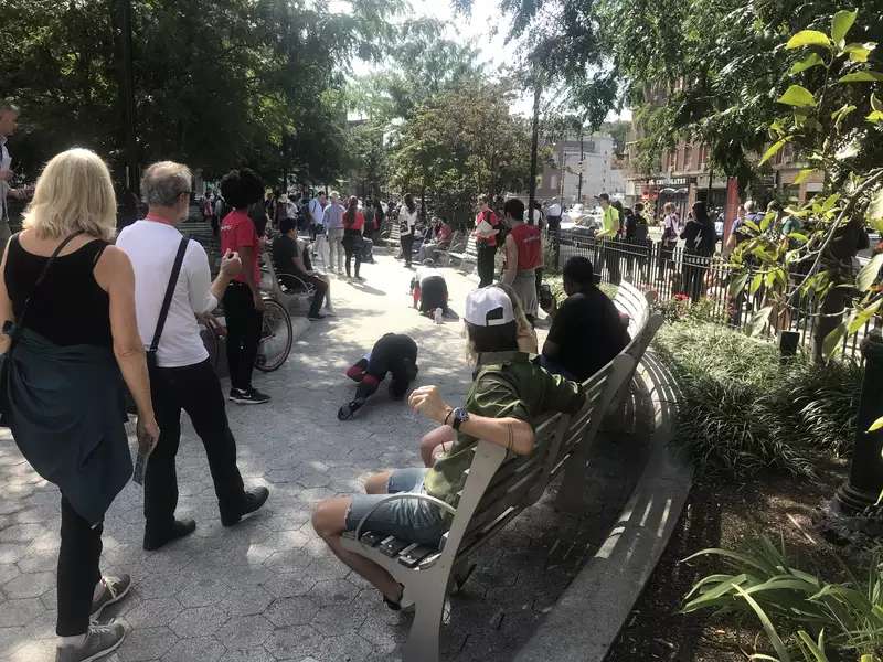 A photograph of Pope.L's Conquest (2019), a group crawl through lower Manhattan that features both performers and audience members. Pope.L is a performance artist well-known for his "crawls," a series of durational performances that the artist describes as experiments in "giving up verticality" and which blur the lines between spectators and performers.