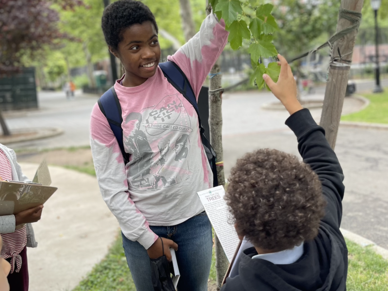 A Barnard student holds a tree branch up to a child as he examines a leaf on the branch