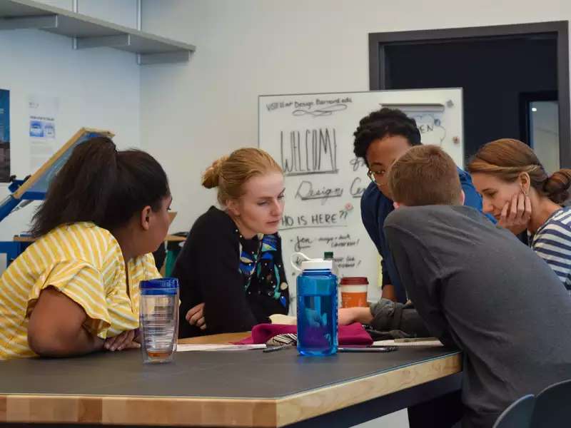 Group of five people seated around table in the design center discussing a project with a staff member