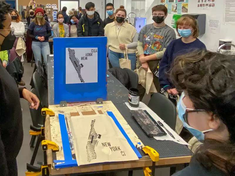 Photo of an event in the design center. The foreground includes staff screen-printing a map of manhattan and event participants are standing in the background.