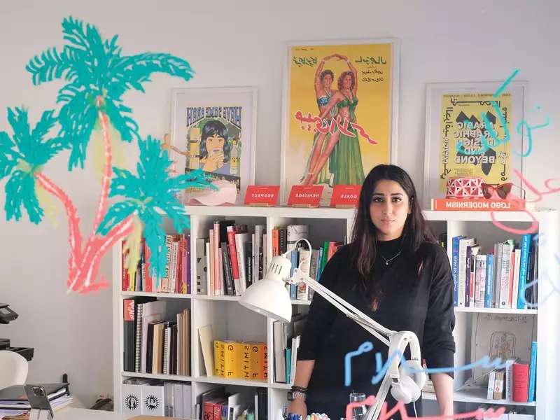 Woman with dark hair and dark shirt standing in front of desk inside a design studio