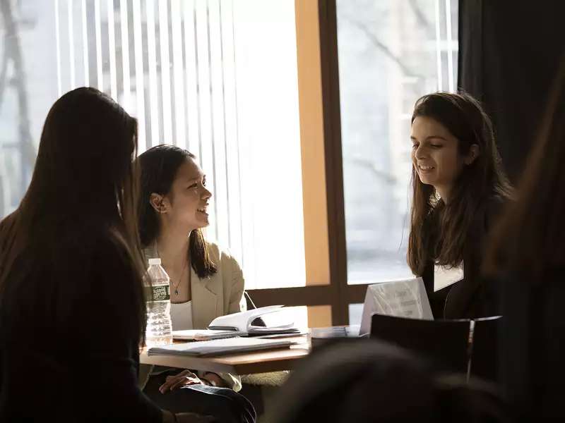 Two students listen as alumna smiles and chats.