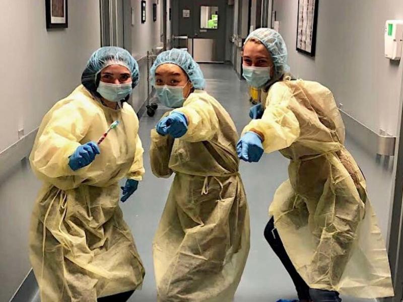 3 young women dressed in surgical scrubs in a hospital hallway, pointing at the viewer
