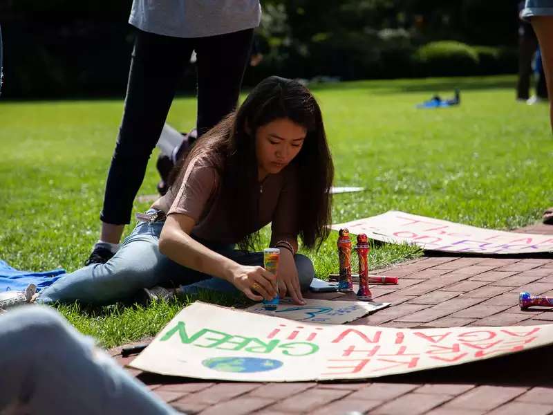 Young woman works on a poster for a climate march on a sunny day