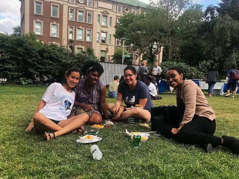 4 women students seated on the grass, smiling