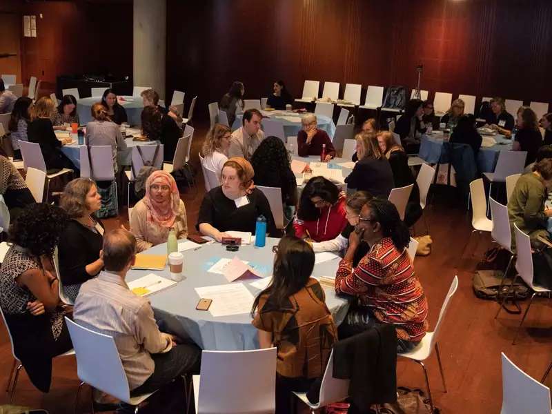 Dozens of women seated at conference tables, speaking avidly to one another