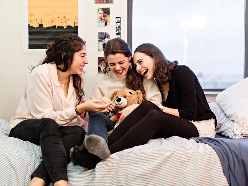 3 students laughing on a dorm room bed