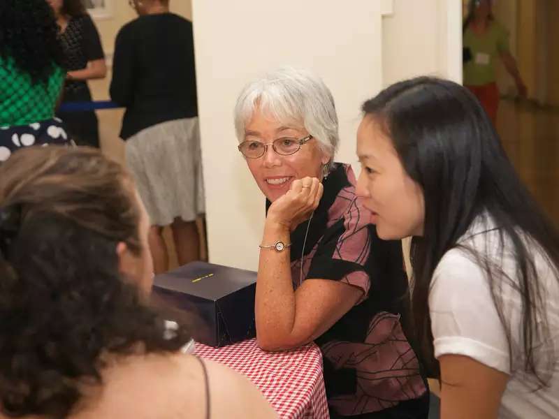 An older alum listens attentively to 2 younger women