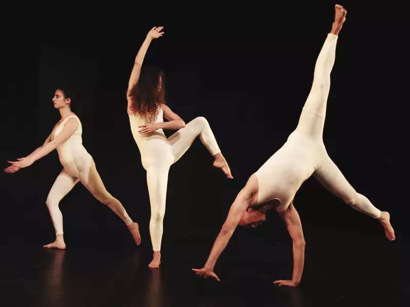3 people in white body suits dancing on a black stage